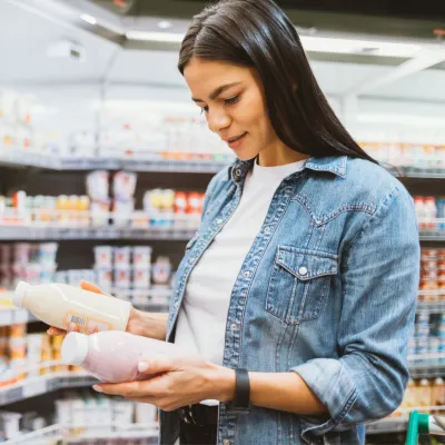 A woman in the dairy aisle of a grocery store holding and looking at bottles.