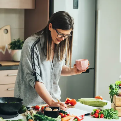 A woman writing down a recipe while in the kitchen and a lot of produce is on the counter.