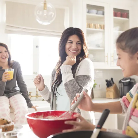 A Caucasian mom dances around the kitchen with her two daughters.