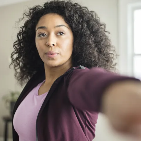 A young African American woman stretches for exercise in her living room.