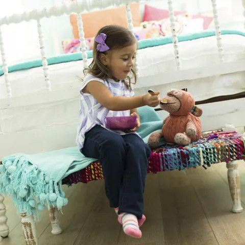 A little girl pretends to feed her stuffed animal in her bedroom