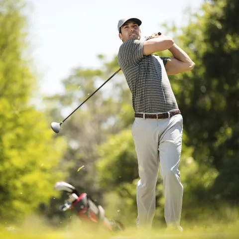A young Caucasian man golfing on a golf course.