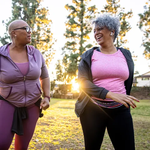 Two Ladies Laugh and Talk as They Walk Through a Park at Sunrise