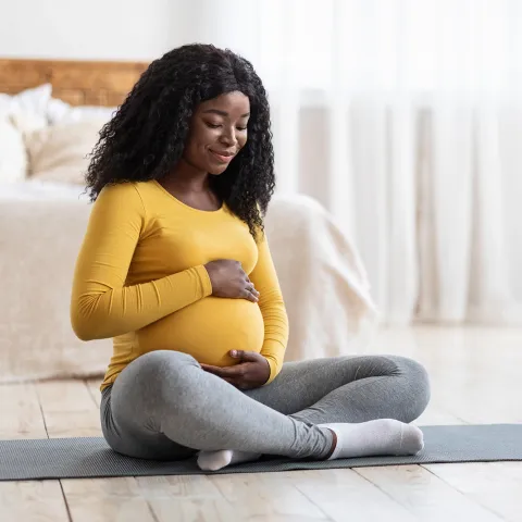 A Woman Sits on a Yoga Mat In Her Bedroom Embracing Her Pregnant Belly.