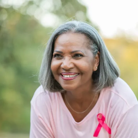 An older woman smiling while wearing a pink shirt and a pink badge