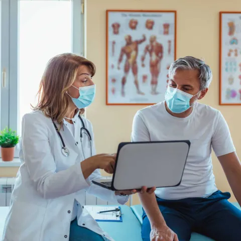 A female doctor pointing at her laptop while showing it to her patient.