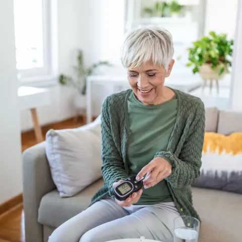A mature woman taking an at-home diabetes test in her living room.