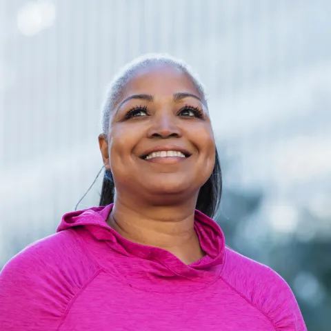 A smiling woman outside wearing a pink shirt for breast cancer awareness.