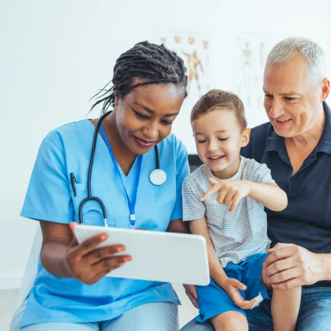 A Doctor Reviews a Patient's Chart with a Pediatric Patient and His Father in an Exam Room.