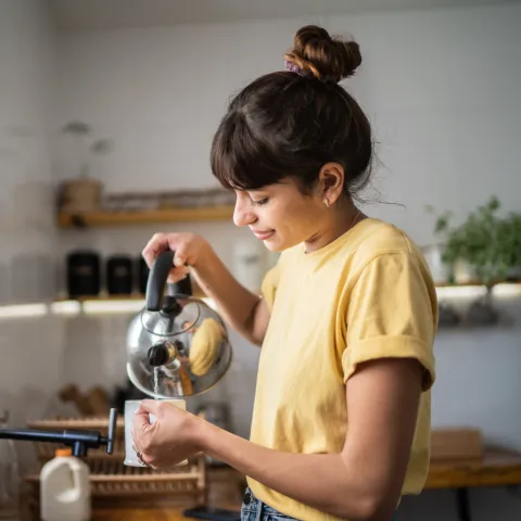 A Woman Smiles as She Pour Hot Water from a Tea Kettle into a Cup
