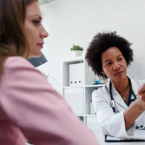 A Doctor Speaks to Her Patient in an Exam Room While Going Over Her Charts.
