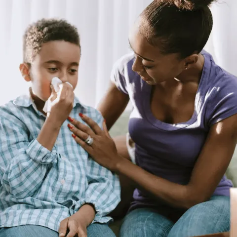A Mother Checks on Her Son as He Blows His Nose at Home
