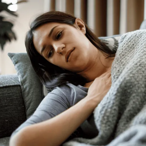 A Woman Lays on Her Couch With Her Hand on Her Chest