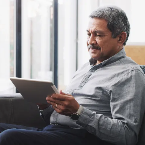 Senior Reading information on a tablet on a sofa
