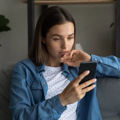 A Young Woman Reads a Message on Her Phone at Home on the Couch