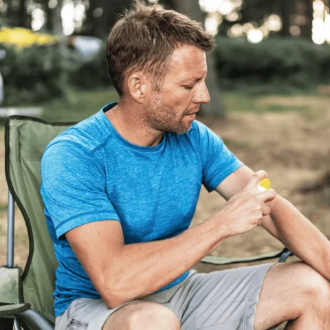 A Man Scratches His Arm While Camping in a Park