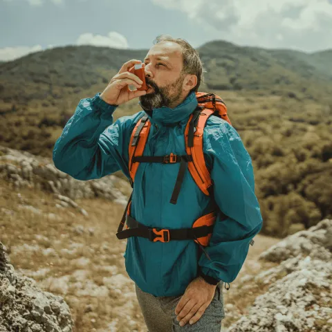 A Man Uses a Inhaler on a Hike Through Rough Terrain