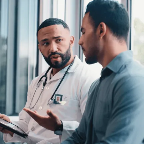 Male patient speaking with male doctor in office.