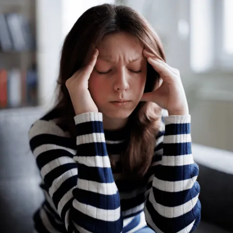 A woman is sitting on a couch with hands resting on the sides of the head.