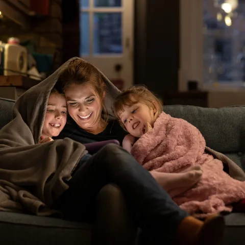 Mother and kids watching videos underneath covers