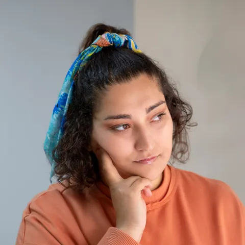 Person wearing an orange sweatshirt rests their chin on their hand, looking thoughtful.