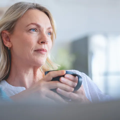 An older woman looking contemplative while sipping a cup of coffee.