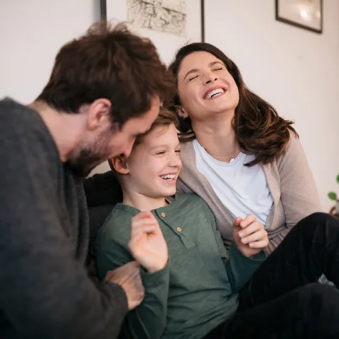 A happy young family sitting on a couch in the living room.