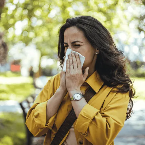 Woman blowing her nose into a tissue outdoors.