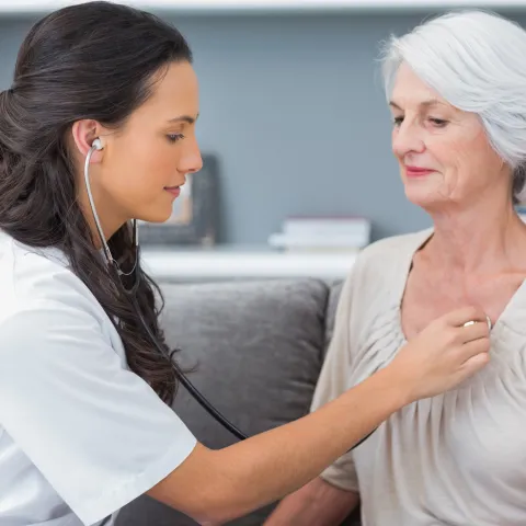 A nurse checks a patient's heart beat as they are both sitting down.