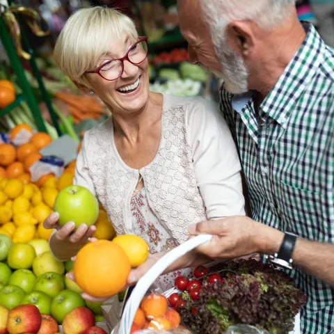 A senior couples shopping for produce with a basket.