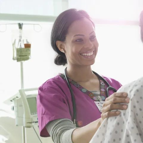 A female African American nurse consoles a woman in a hospital gown.