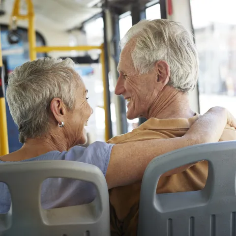 An elderly Caucasian couple rides on the bus on a sunny afternoon.