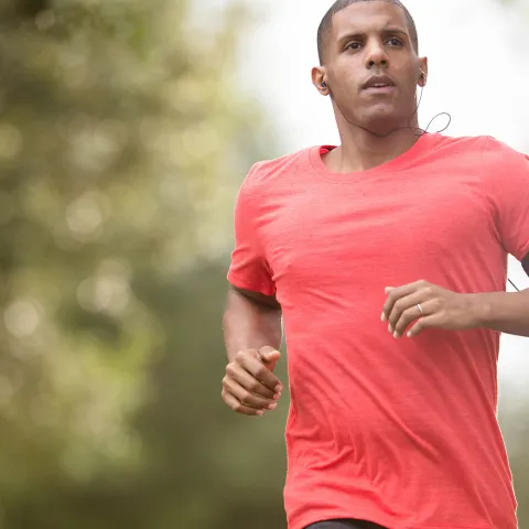 Man in a red shirt running outside while listening to music.