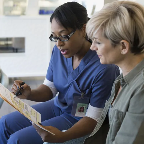 An African American nurse consults with a Caucasian female regarding her diagnosis.