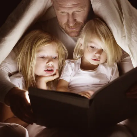 A dad reads to his daughters by flashlight.