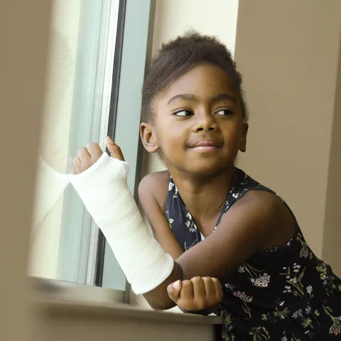 A little girl in a cast smiles while sitting next to a windowsill