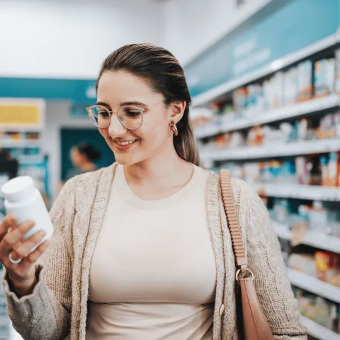 A woman looking at a medication bottle in a store.