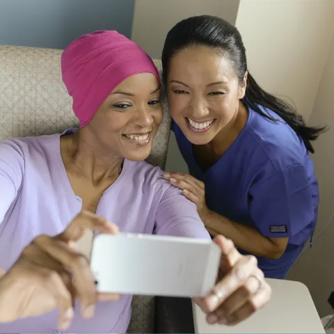 A female African American cancer patient takes a selfie with a female Asian nurse.