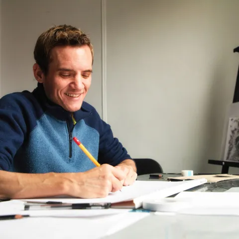 A man drawing with a pencil at a desk.