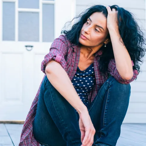 A woman sitting on the porch looking concerned.