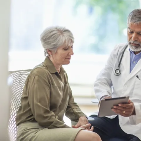 senior man doctor medical professional talks using digital tablet to senior woman in health clinic - stock photo
