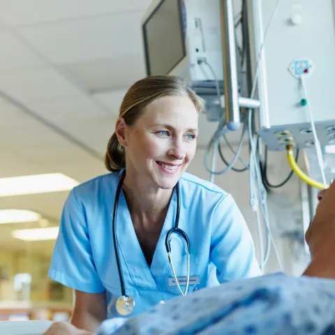 A smiling female physician reassures her male patient in a hospital room.