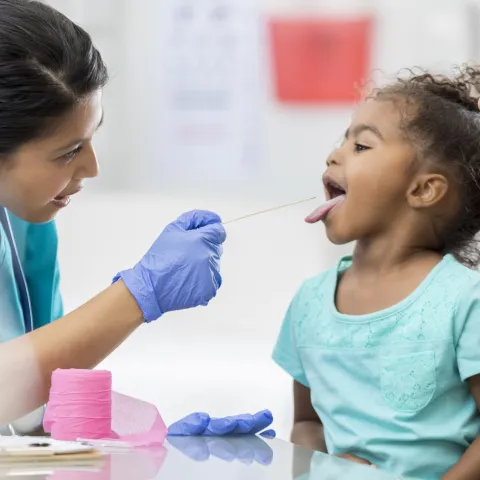 Little girl sitting on her mother's lap sticking her tongue out for the doctor.