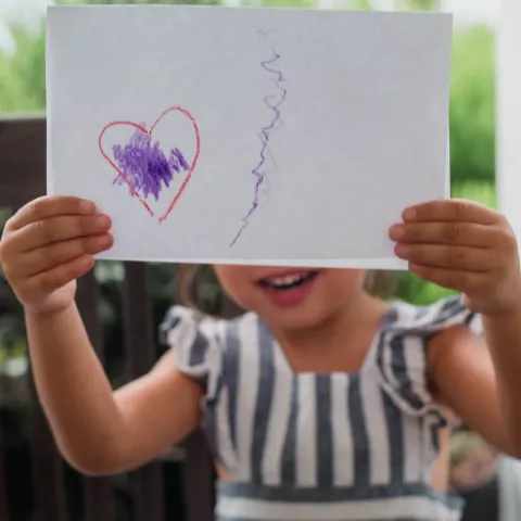 A little girl proudly displays her artwork for the camera.