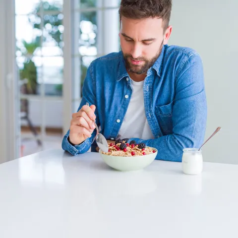 A gentleman eating a bowl of cereal with berries and a cup of yogurt