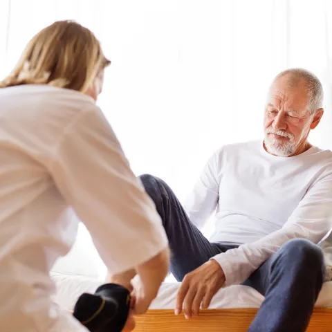 A senior gentleman being assisted in putting his socks on.