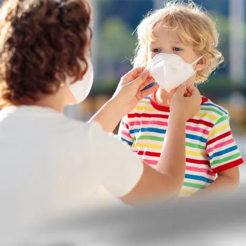 A mom helps her son position his face mask.