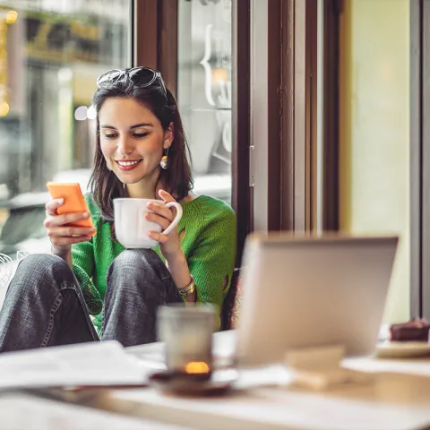 Hispanic woman with tea holding her phone and smiling.