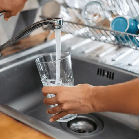 A drinking glass being filled from a tap.