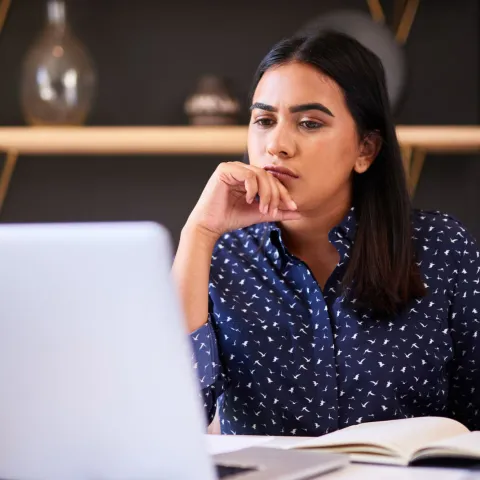A woman looking thoughtfully at her laptop